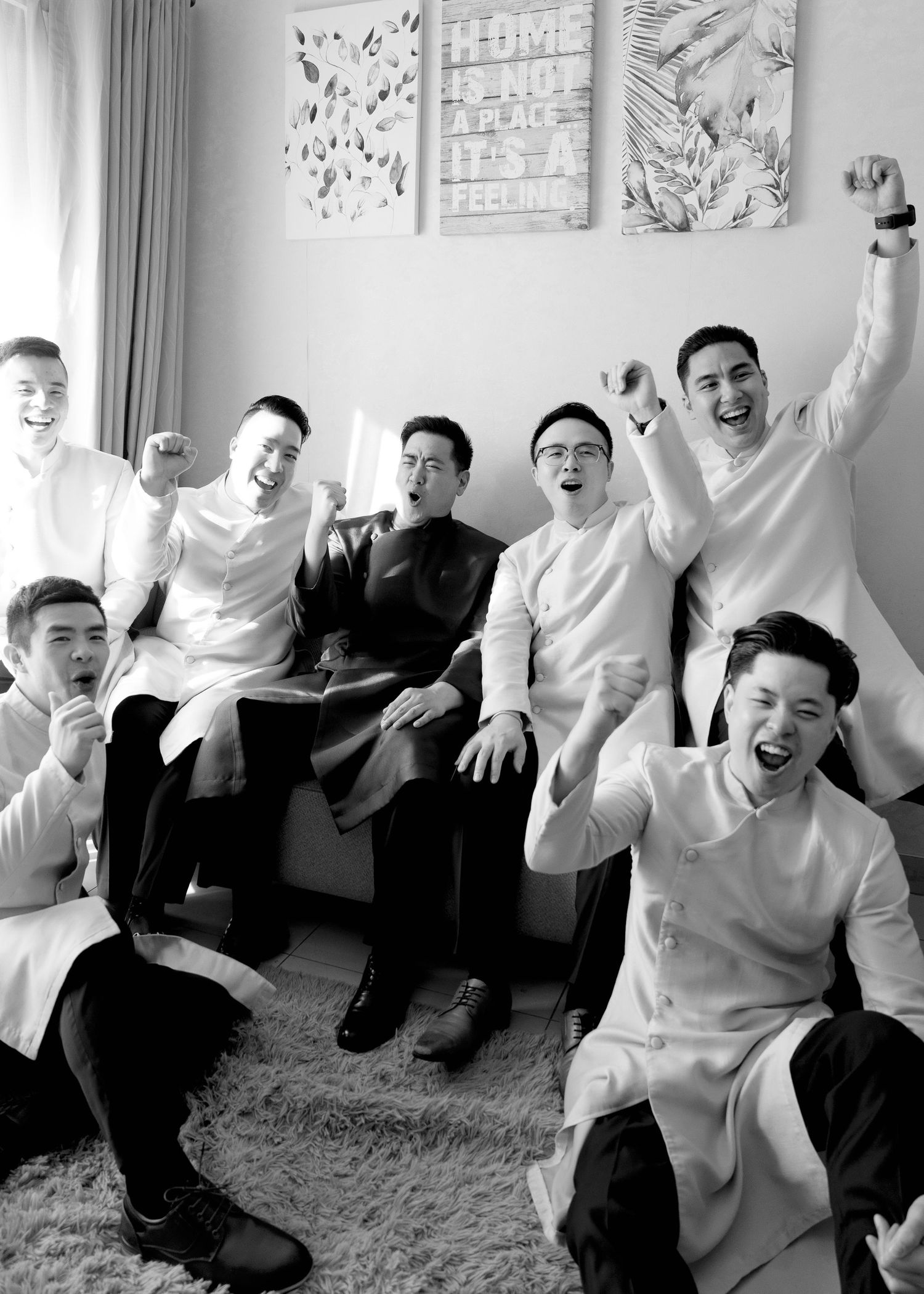 Black and white photo of groom and groomsmen cheering joyfully in traditional Vietnamese ao dai.