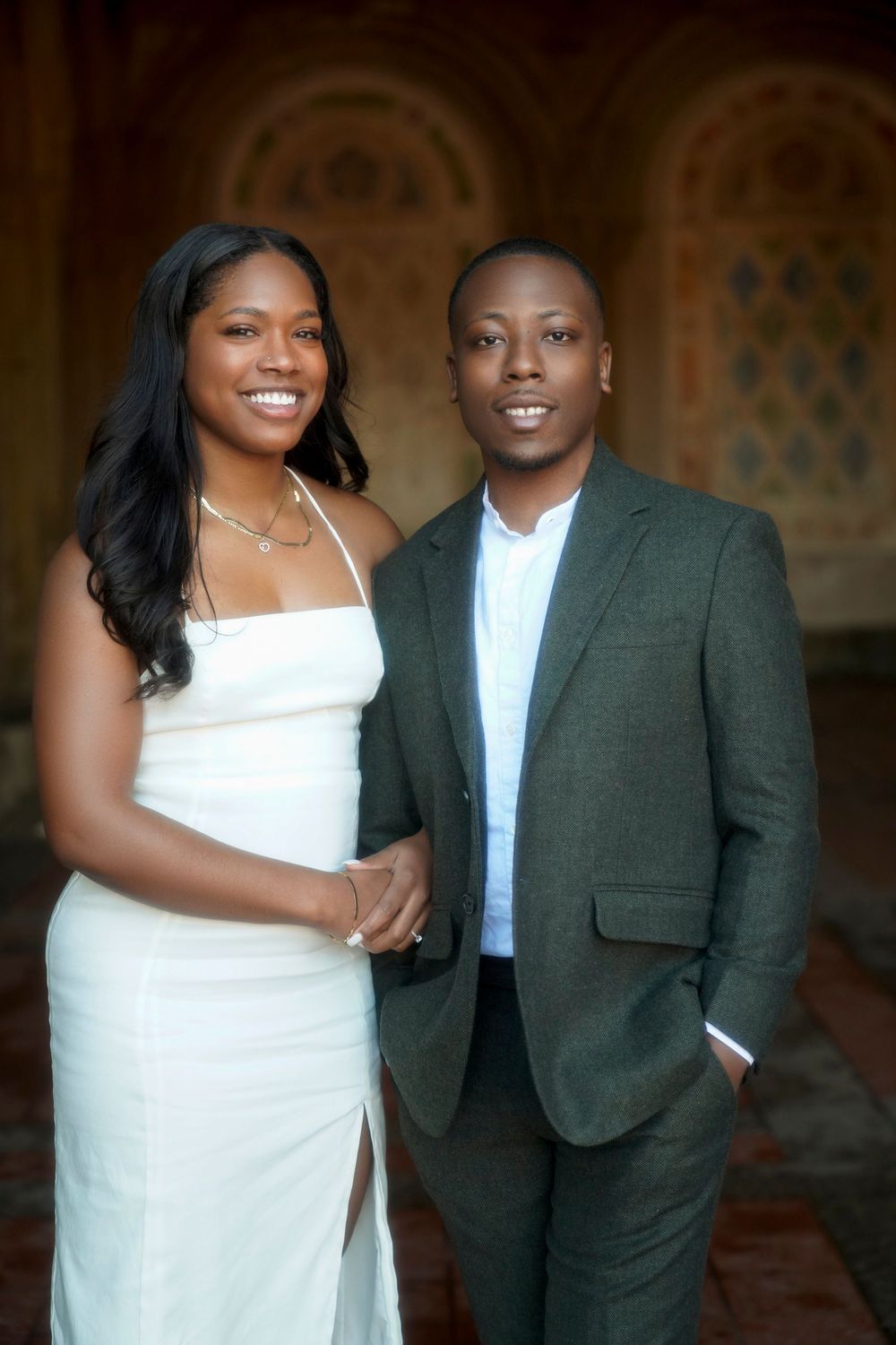 A couple shares joyful candid moments in formal attire against a dark backdrop during their photoshoot. Bethesda Terrace