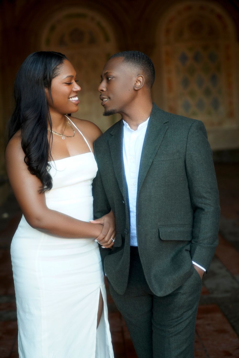 A romantic couple in white dress and grey suit share tender moments in a series of candid engagement photos. Bethesda Terrace