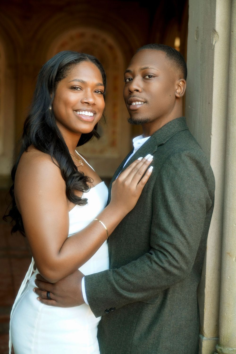 Intimate engagement photo of a couple embracing in formal attire against an elegant arched backdrop. Bethesda Terrace