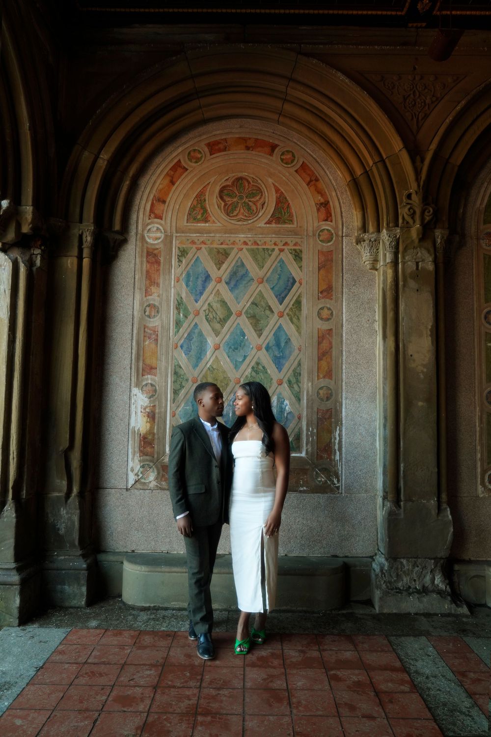 Formal couple poses elegantly in front of an ornate archway with decorative blue diamond patterns and terra cotta tiles. central park