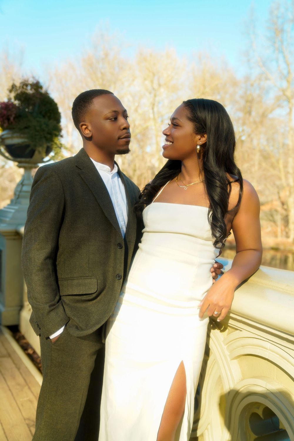 A couple sharing a romantic moment in formal attire on a wooden deck with autumn trees in the background. central park