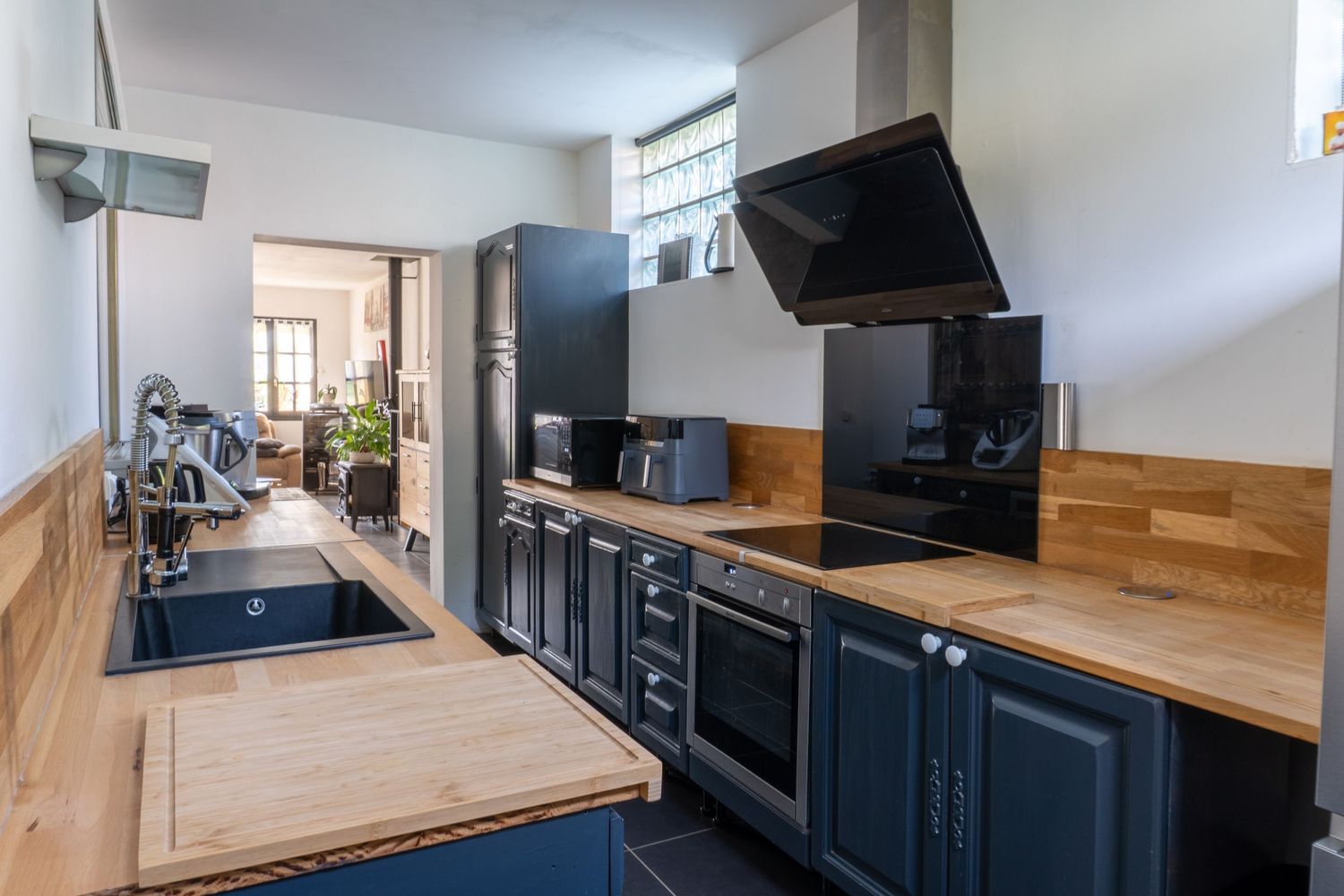 Modern kitchen interior with blue cabinets, wooden countertops and black appliances in a galley-style layout.
