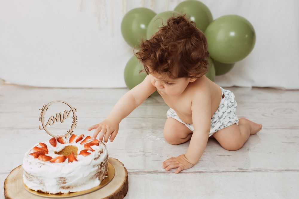 Birthday cake smash photography setup with green balloons and white backdrop.