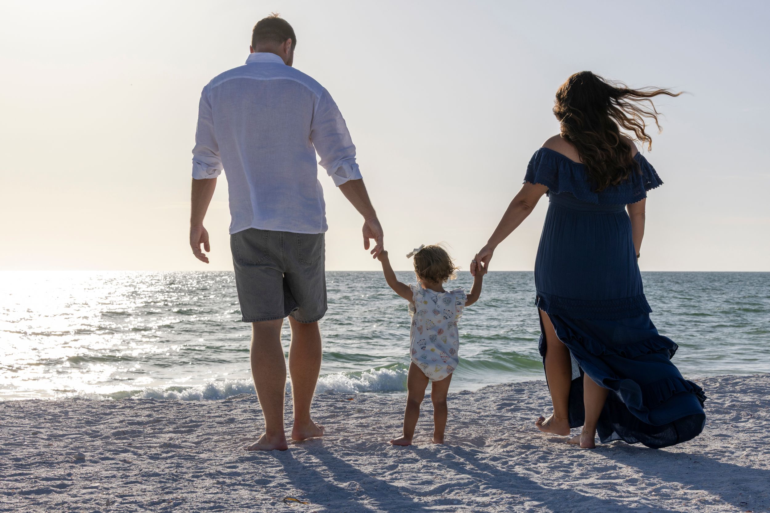 Family walking together on a sandy beach at sunset with ocean waves in the background.