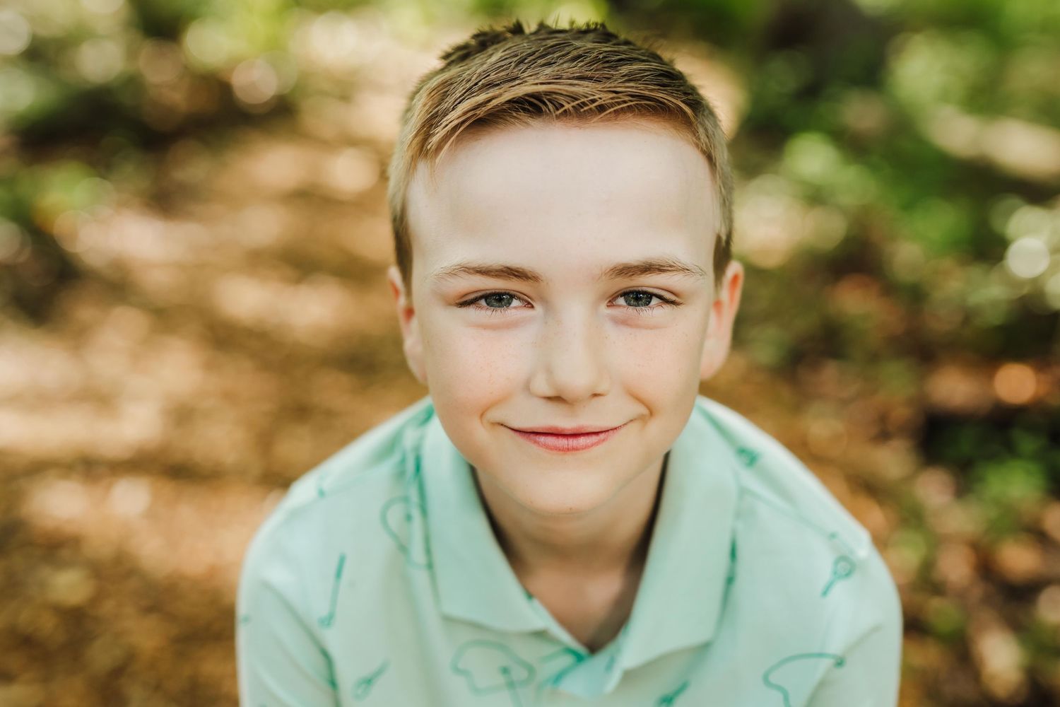 A happy young person in a mint green polo shirt smiles at the camera while outdoors in natural lighting.