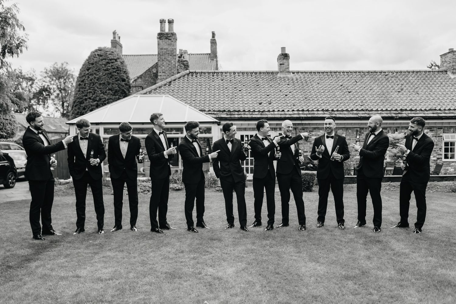 Large group of formal wedding attendees lined up outside in black suits and formal attire.