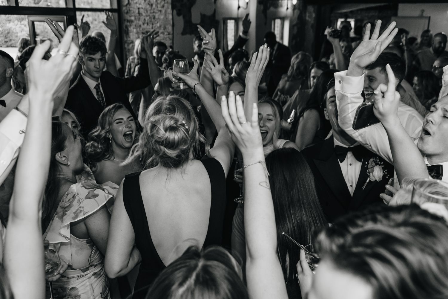 Wedding reception crowd with raised hands dancing and celebrating on a dance floor in black and white.