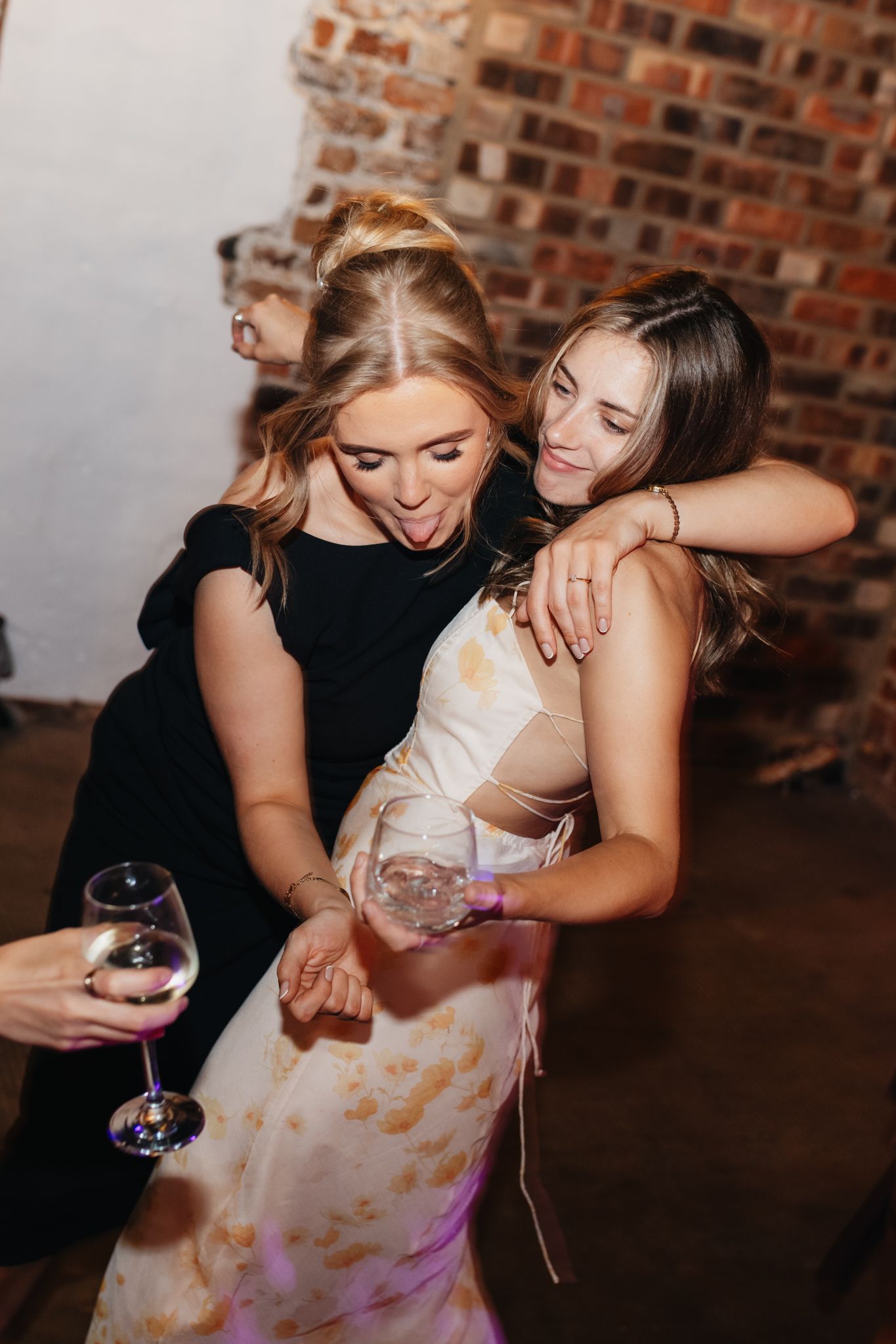 Group of friends in dark attire celebrating and laughing at reception party against brick wall.