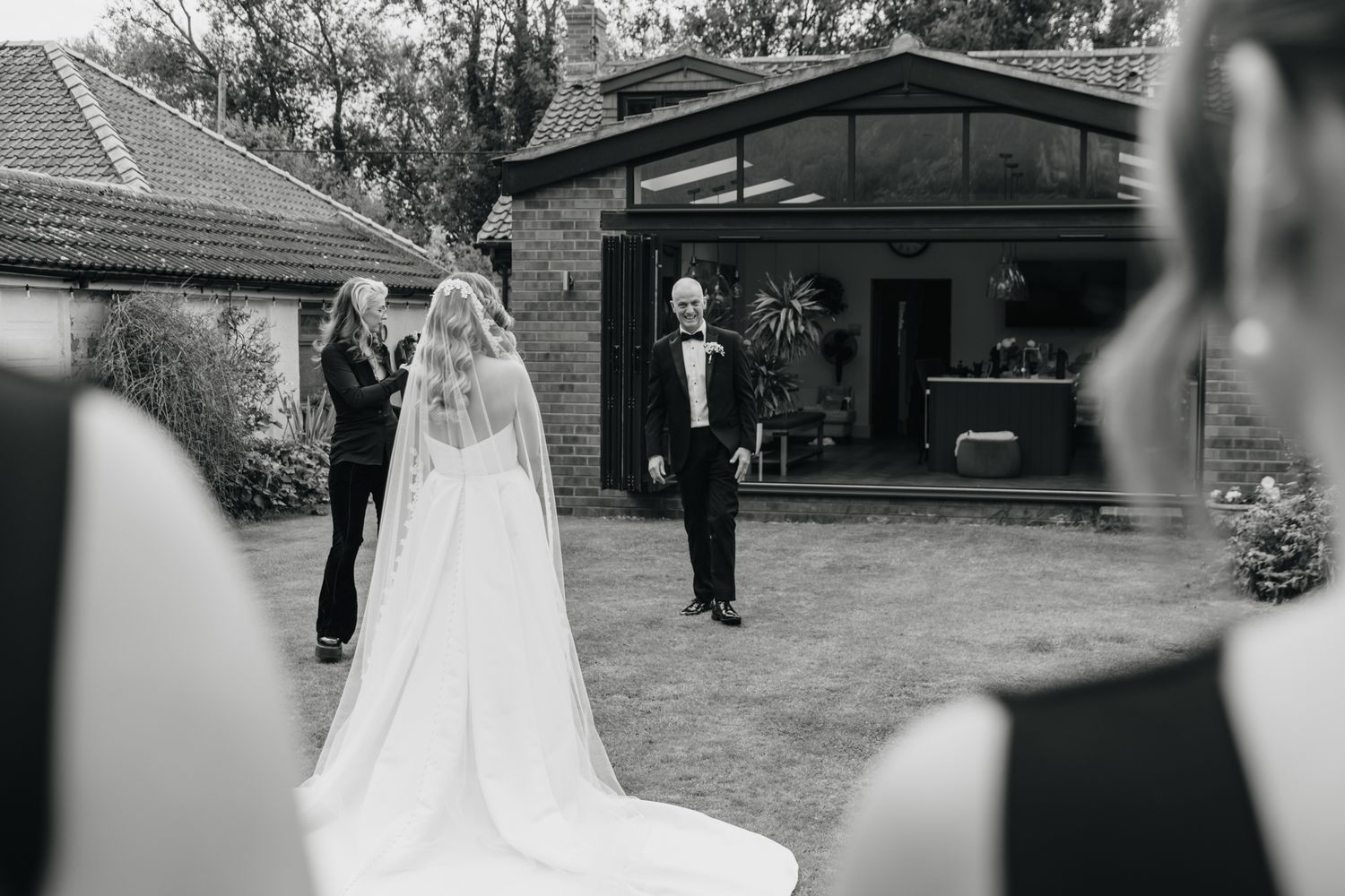 Wedding guests gather outside a venue's brick building on a bright sunny day.