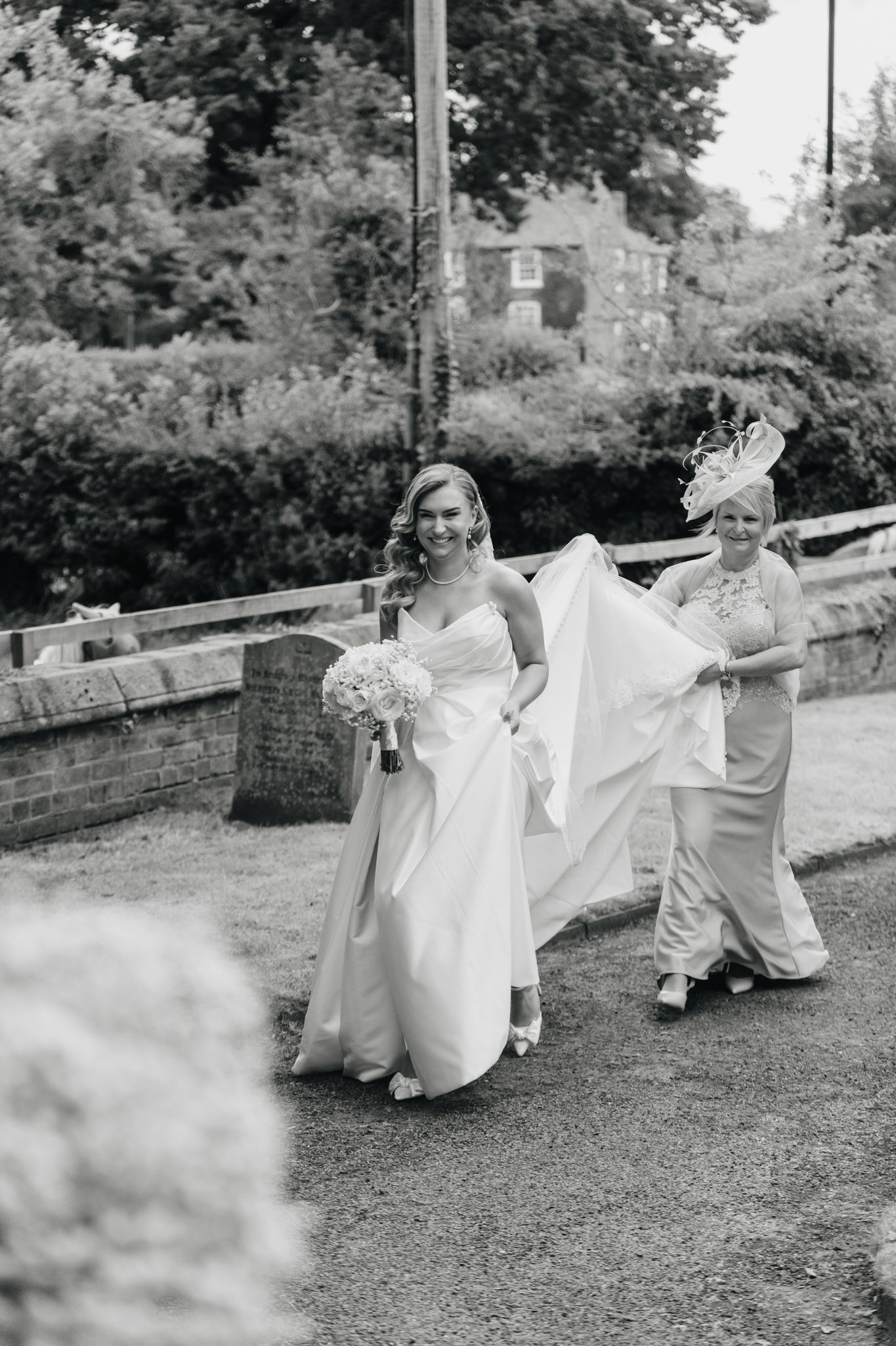 Wedding party having fun outdoors on a lawn while holding the bride's dress train.