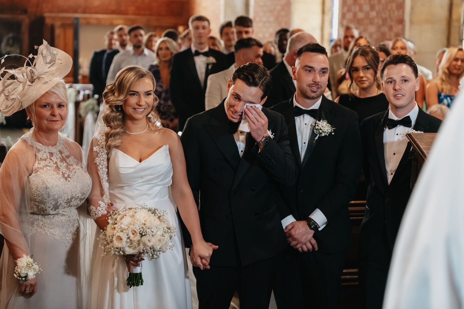 Wedding party lineup in a grand hall with bridesmaids in blush dresses and groomsmen in black tuxedos.
