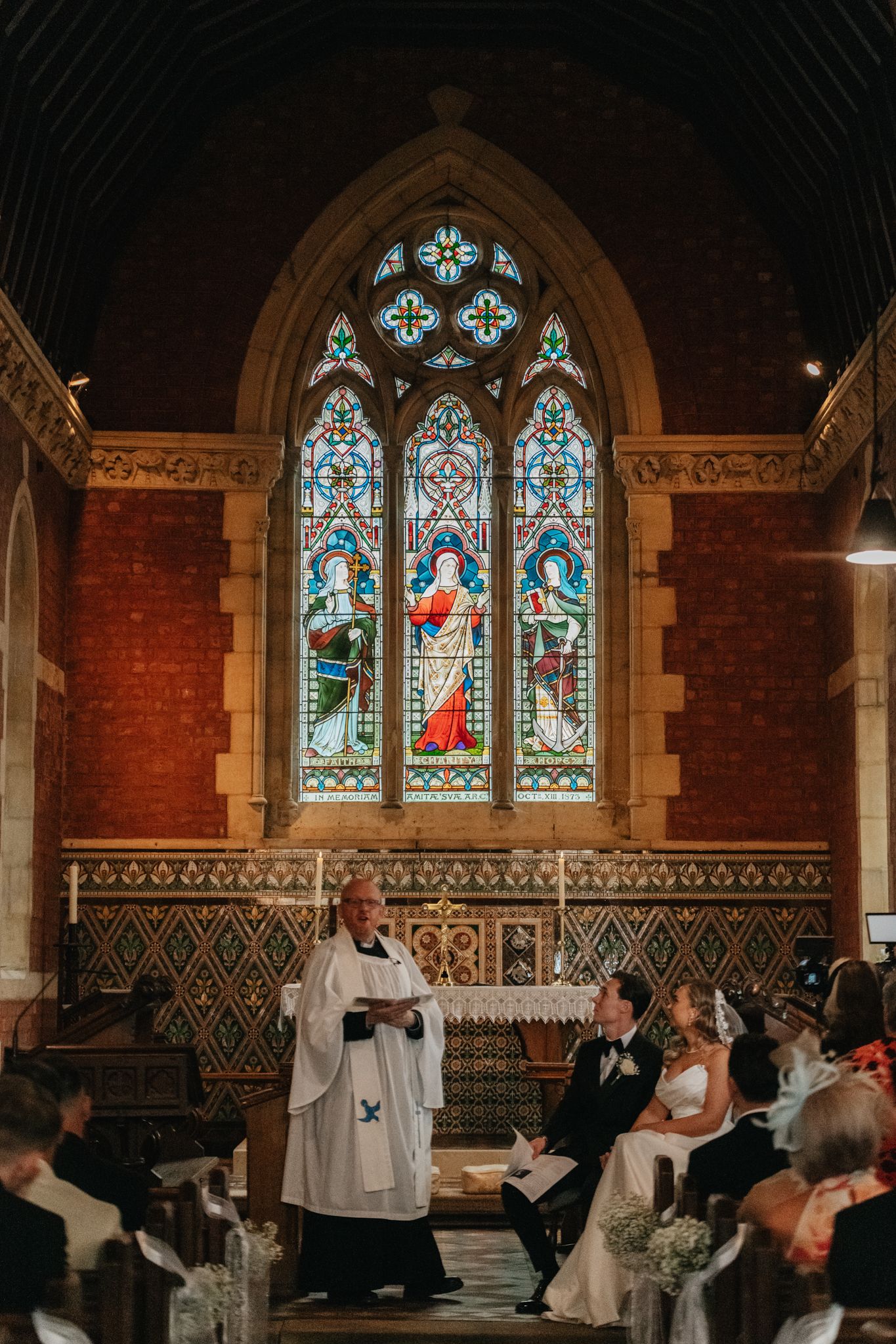 Wedding ceremony in historic church with beautiful stained glass windows and brick walls.