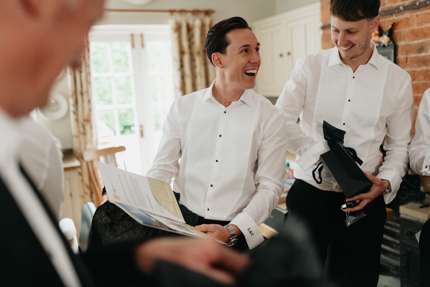 Groomsmen in white dress shirts share joyful laughter while getting ready for a wedding celebration.