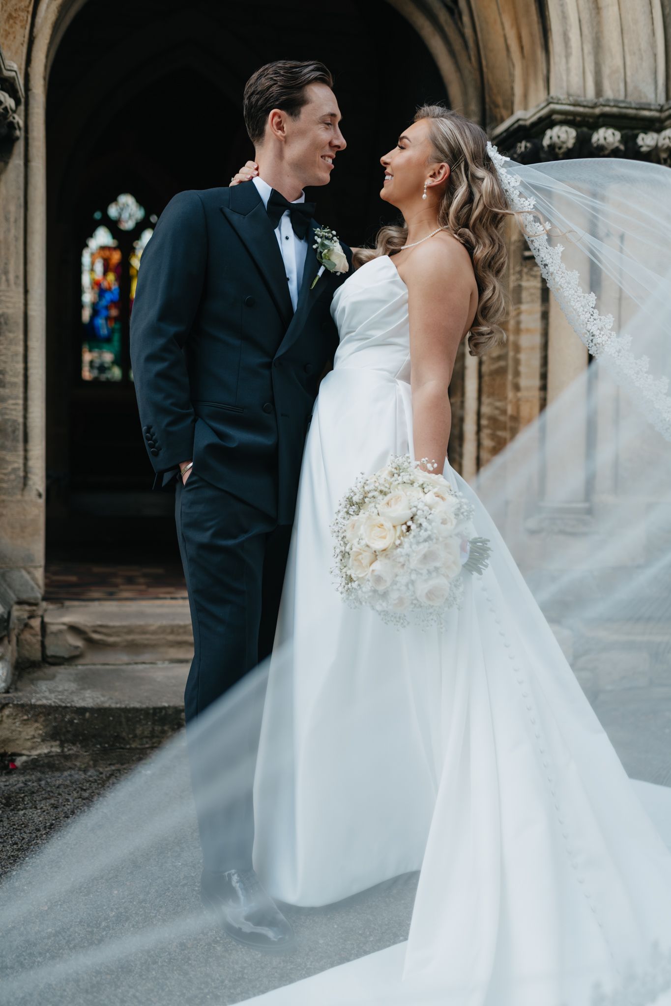 Elegant bride in flowing white gown with veil dancing with groom in black tuxedo.