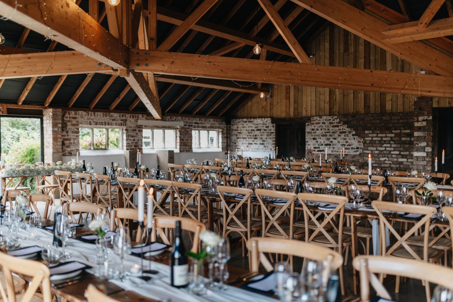 A rustic barn wedding reception venue features elegant table settings and wooden beams in a spacious interior.