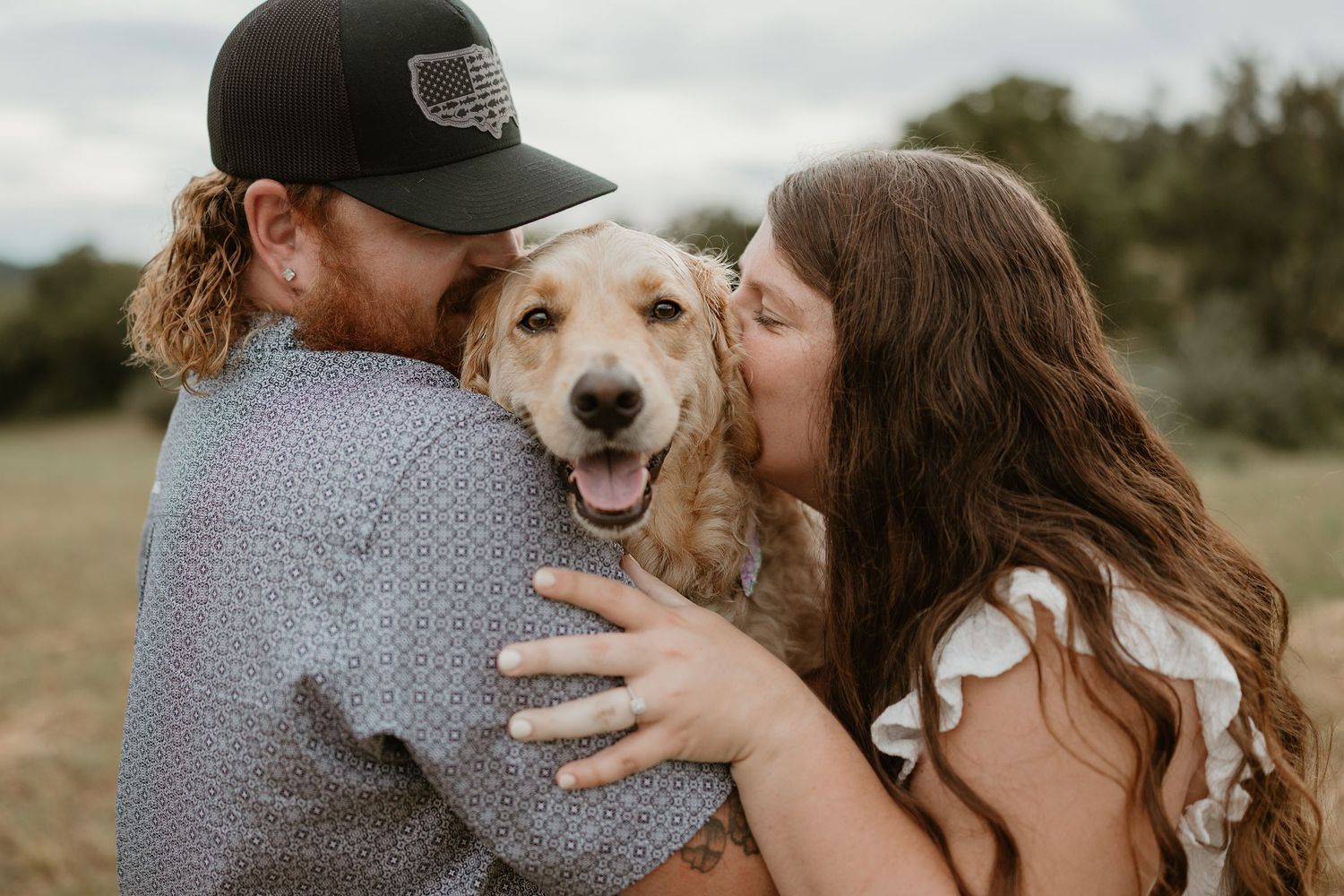 Happy dog receives loving kisses from owners in outdoor portrait session.