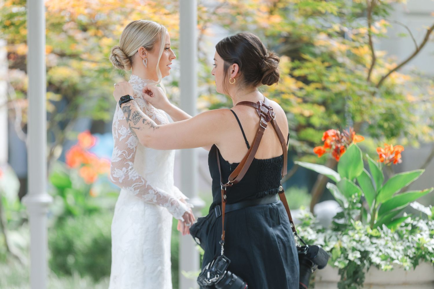 Two people dancing together in an elegant outdoor wedding reception with greenery and string lights in the background.