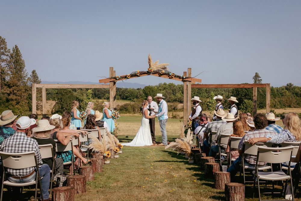 Outdoor ranch wedding ceremony with bride and groom under wooden arch – Vancouver WA wedding photography.