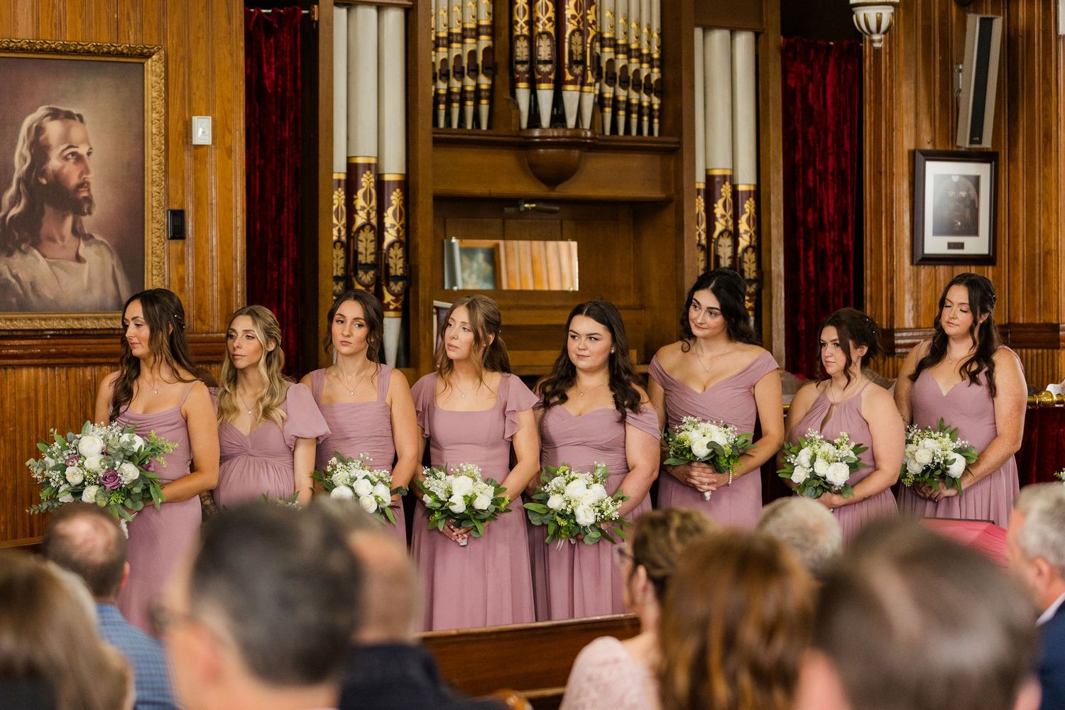 A group of bridesmaids in pink dresses stand in a row at a church wedding ceremony.