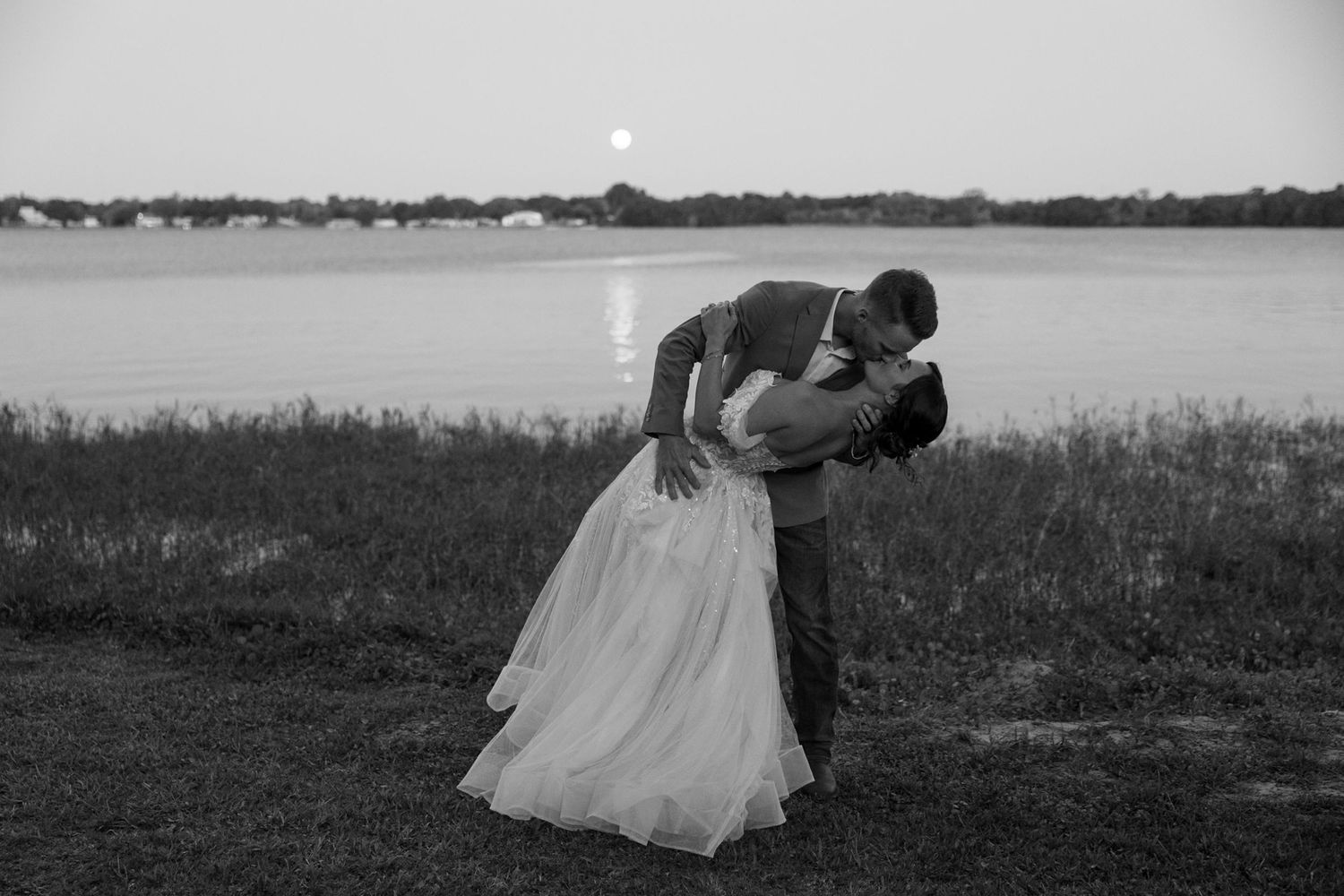A series of black and white photographs showing wedding moments on a grassy field near the water.