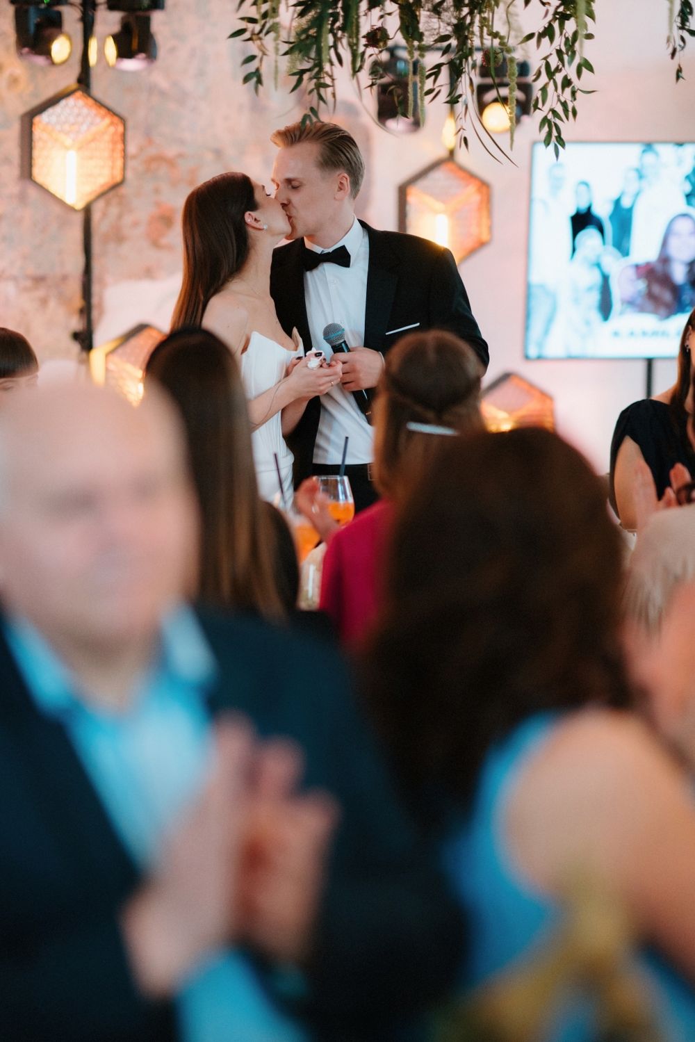 Celebration in a rustic venue with pink-tinted walls and hanging botanical decorations.