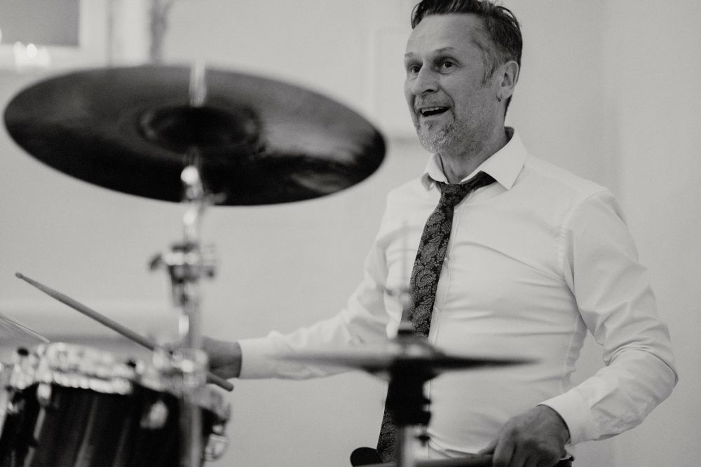 Musician playing drums with enthusiasm during wedding reception performance.