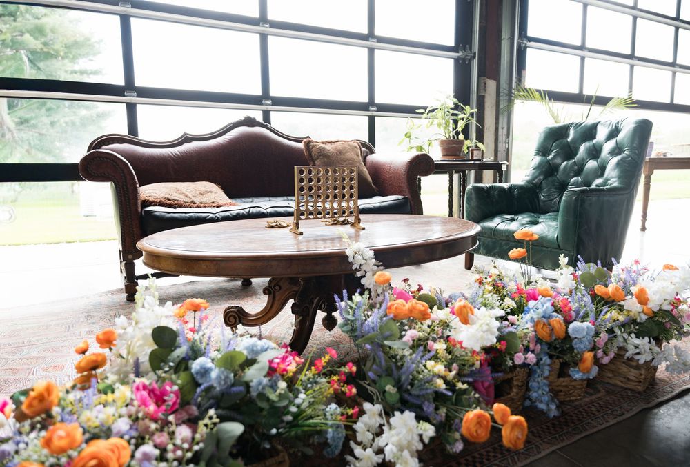 A vibrant floral centerpiece with mixed blooms adorns a wooden table setting with natural window lighting.