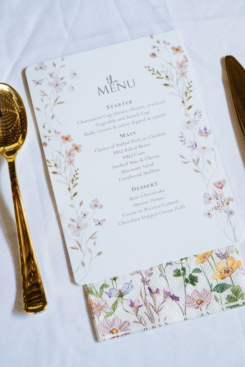 Elegant wedding menu cards with delicate floral watercolor designs and gold cutlery on white linen.