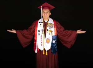 Graduate in red cap and gown with decorated stoles and arms outstretched against dark background.