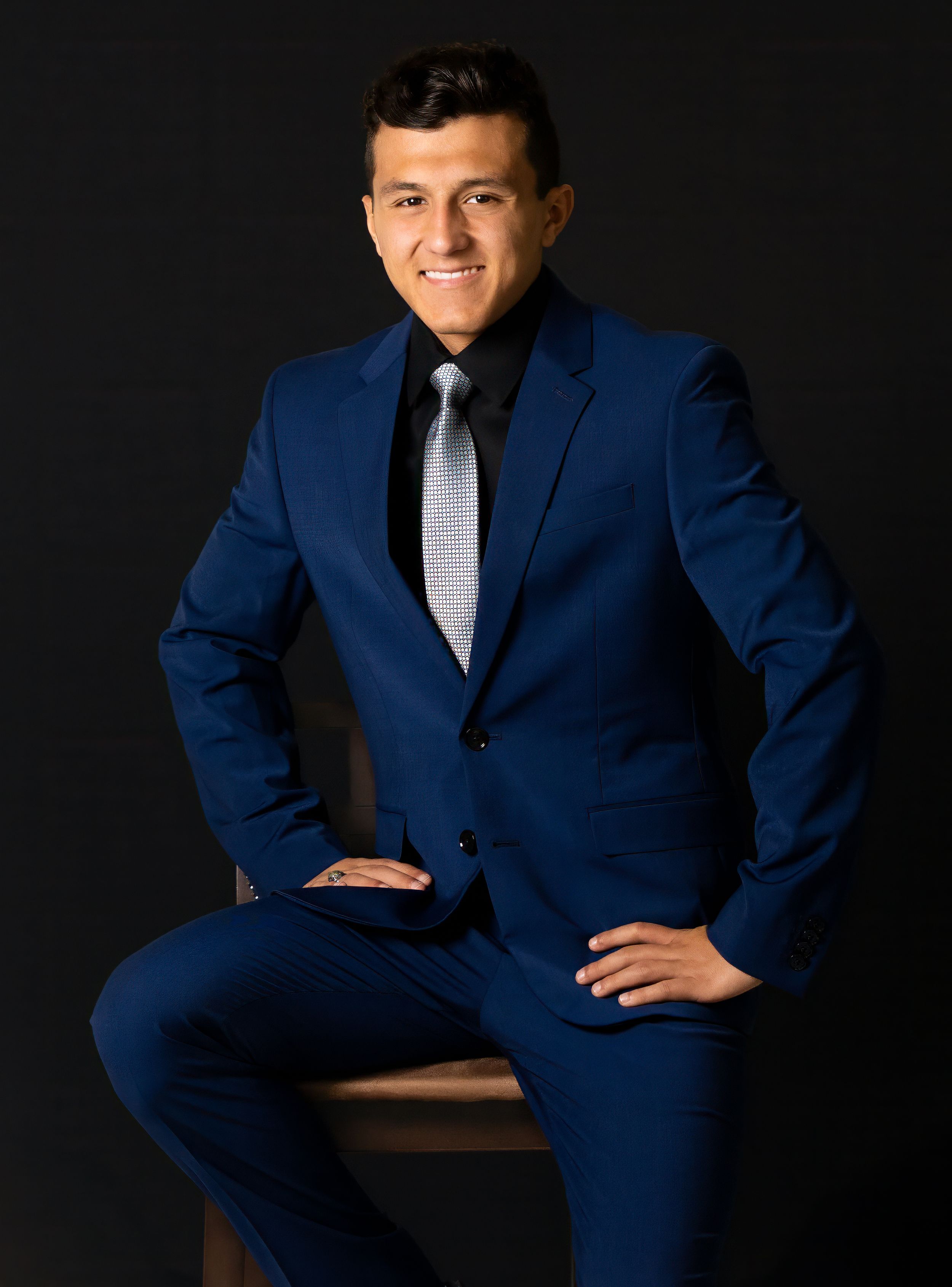 Professional portrait of person in navy blue suit seated on dark background.