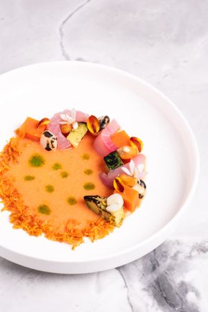 White fish tiradito decorated with colorful garnishes and microgreens on a white plate.