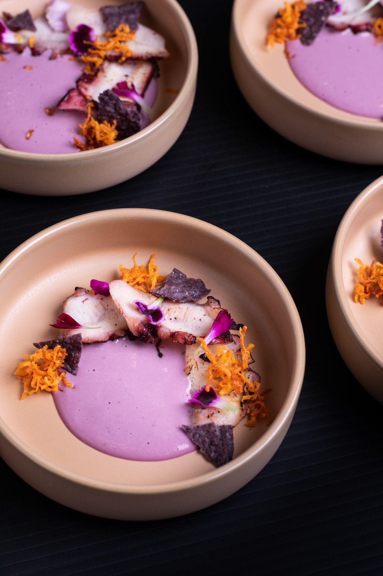 Grilled octopus bowls garnished with orange zest and edible flowers in ceramic dishes.