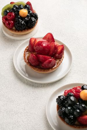 Fresh fruit tarts topped with colorful berries and arranged on white plates.