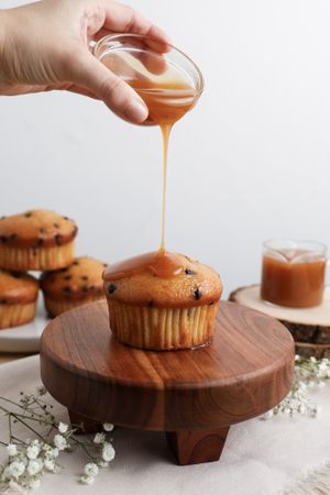 Caramel sauce being drizzled over chocolate chip muffin on wooden serving board.