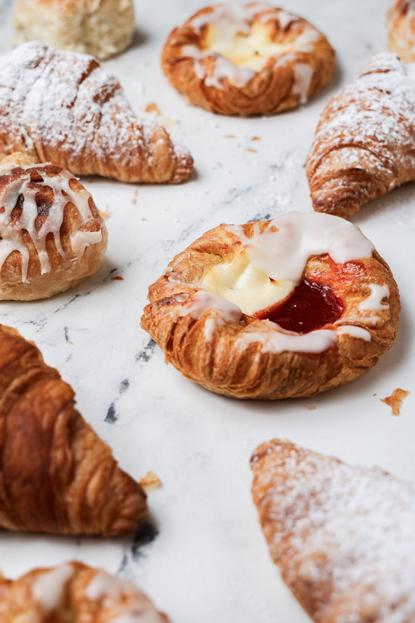 Assorted fresh Danish pastries and croissants dusted with powdered sugar.