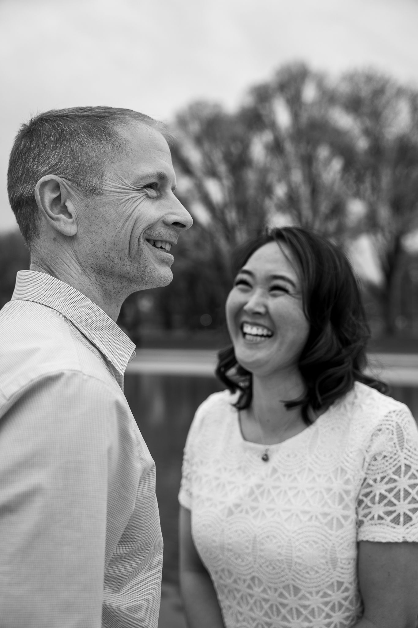 A candid black and white portrait of a couple laughing together outdoors.