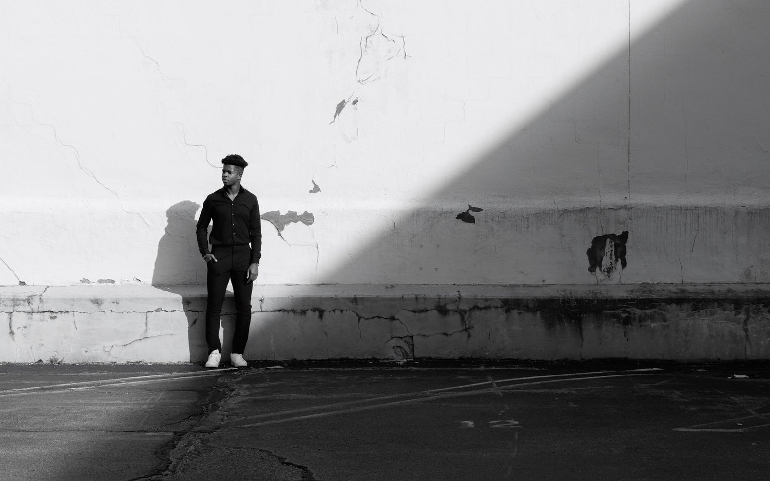 A silhouetted figure stands against a stark white wall casting dramatic shadows.
