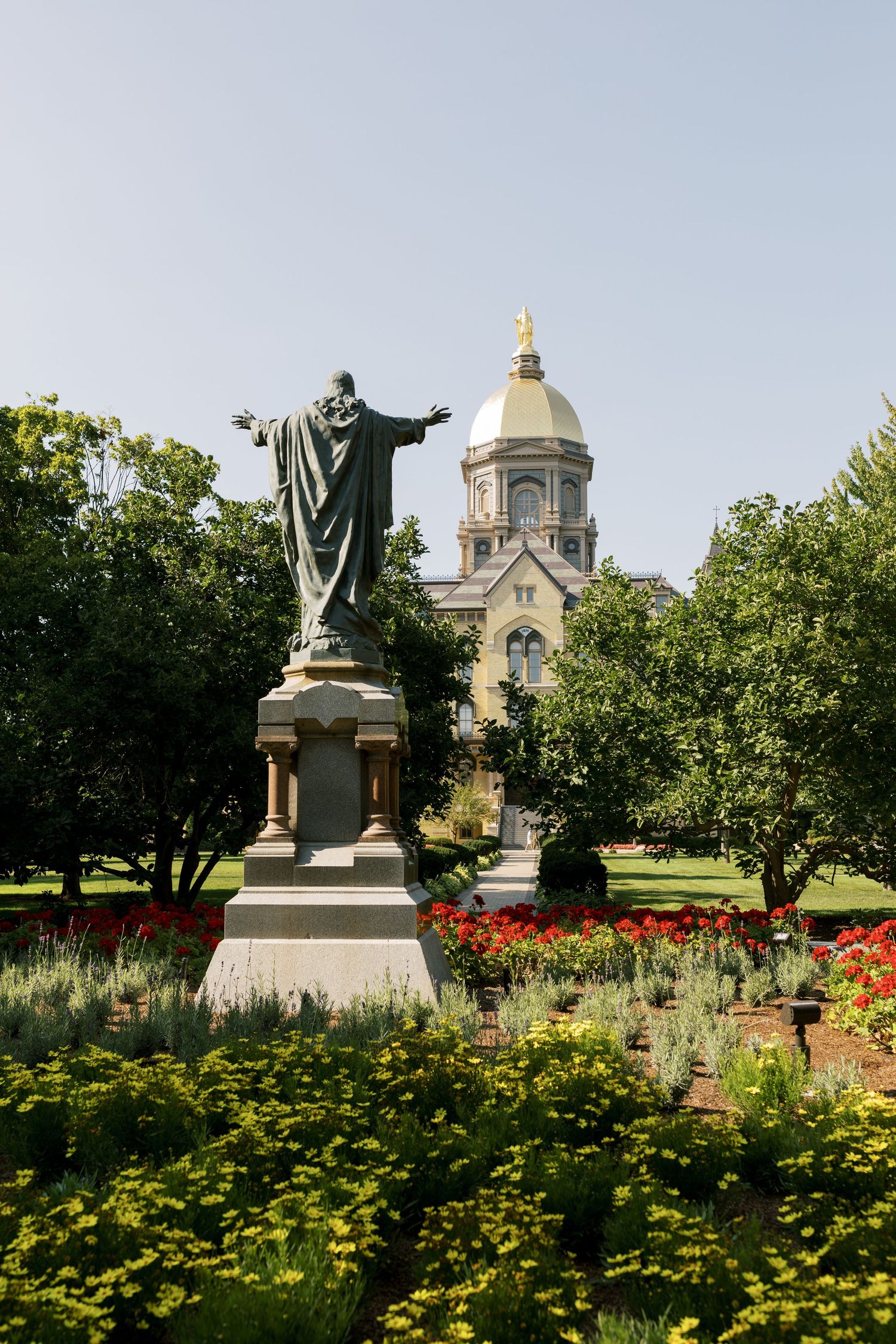 The golden dome of Notre Dame behind a bronze statue surrounded by vibrant flower gardens.