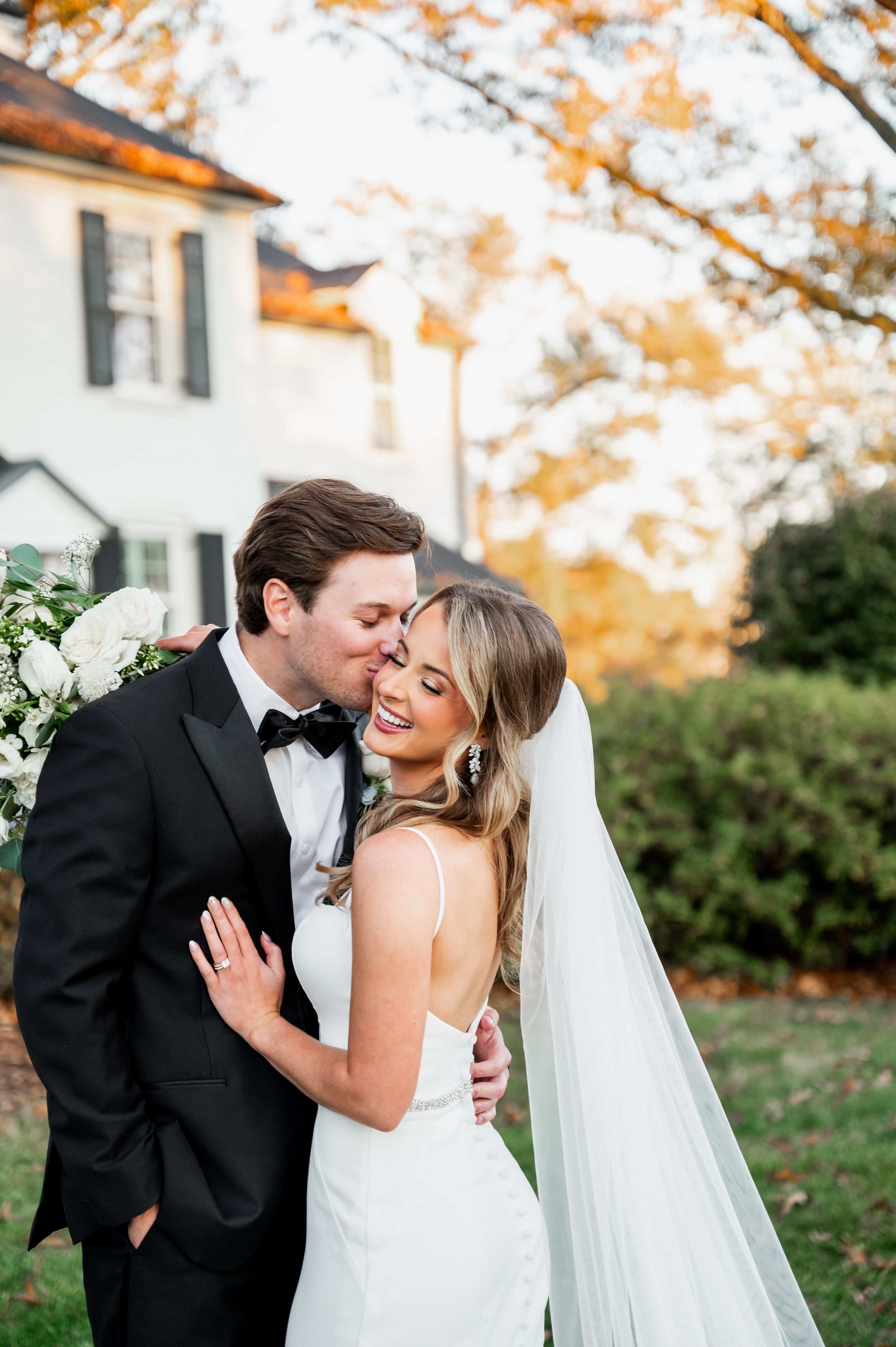 Autumn wedding portraits with couple sharing intimate moments against fall foliage and white house.