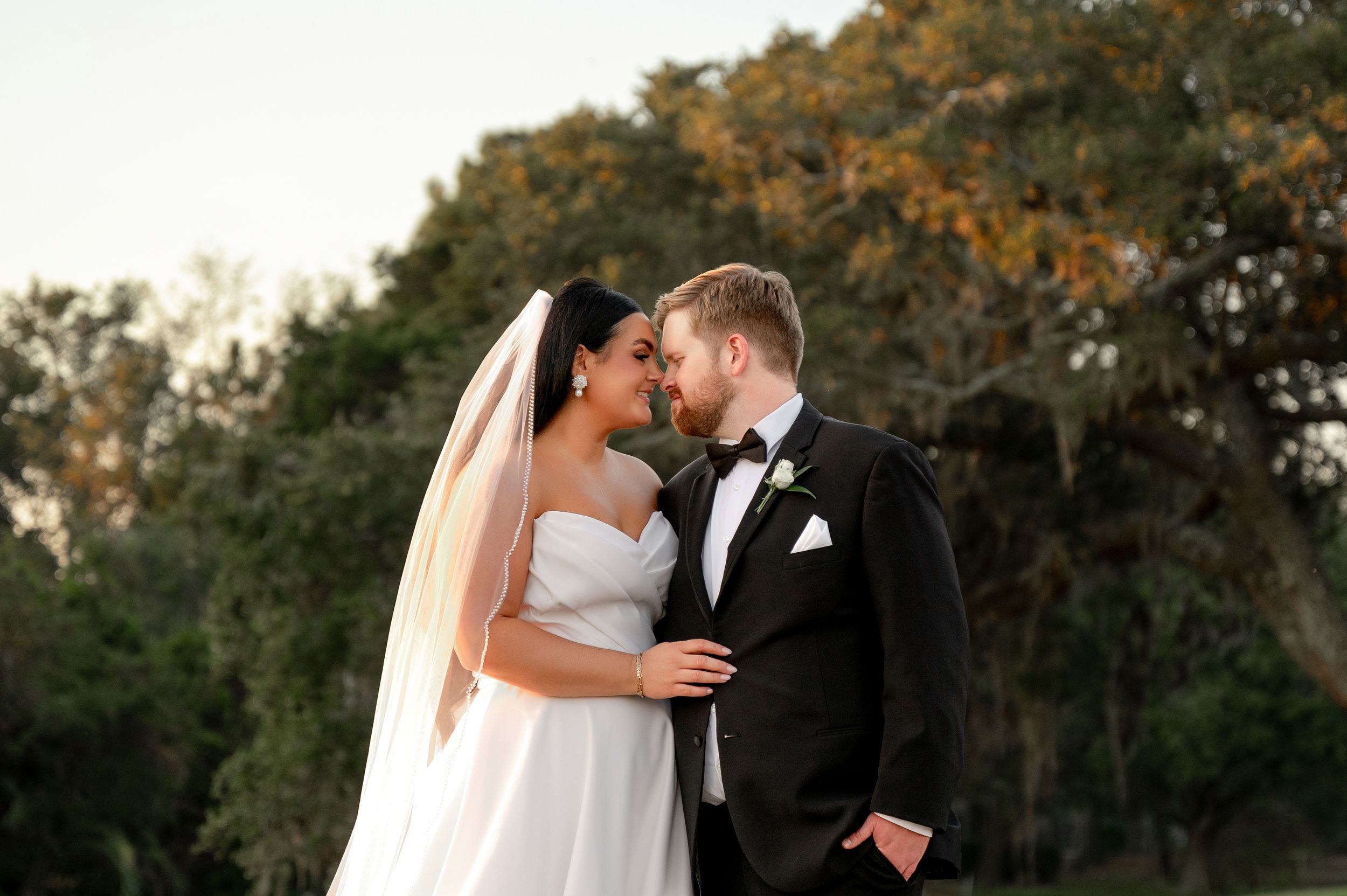 Couple shares romantic sunset moment in garden setting with flowing bridal veil.