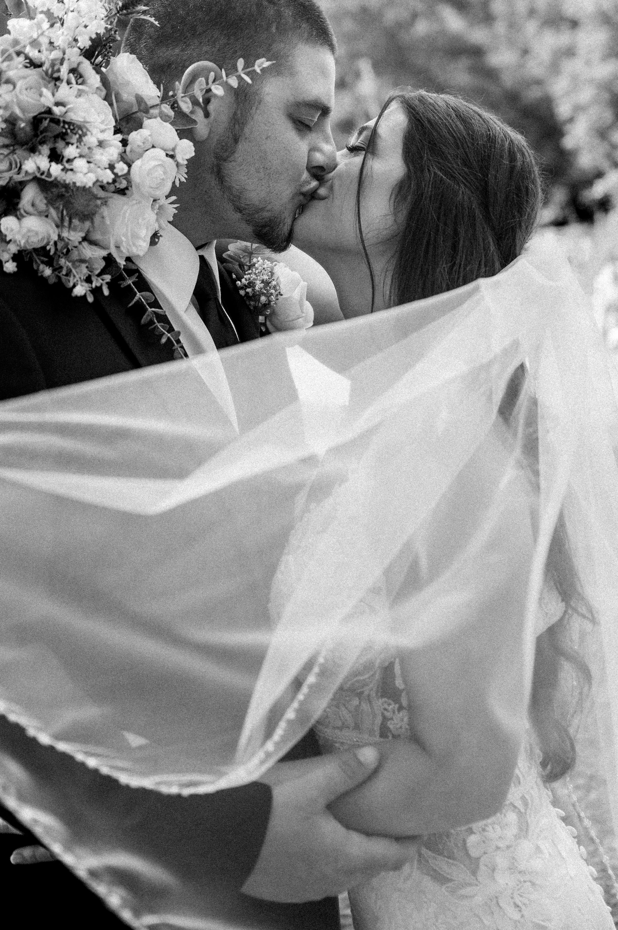 Black and white wedding portrait with flowing veil creating romantic movement.