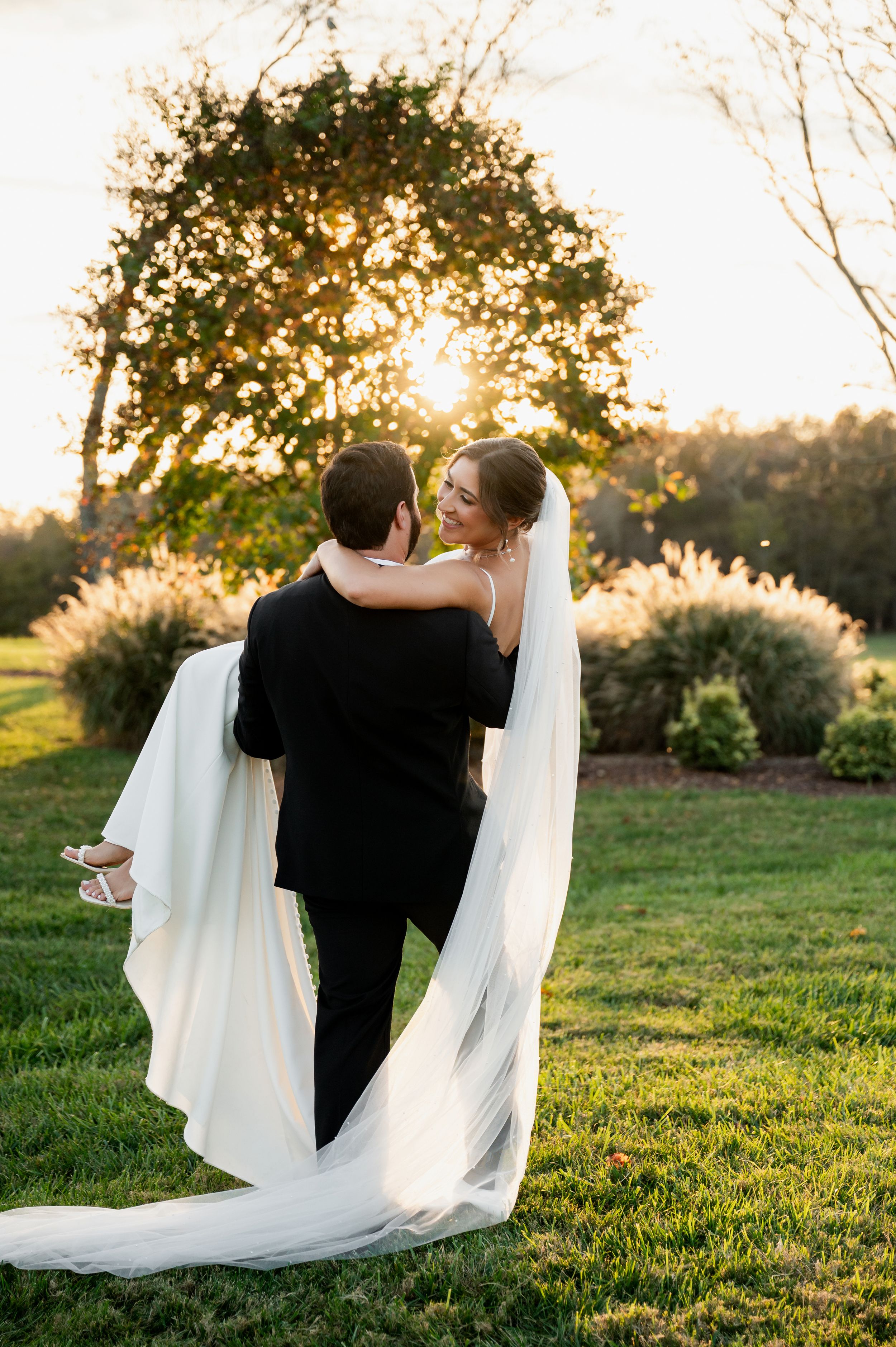Newlyweds share intimate moment on grassy hill during golden hour sunset.