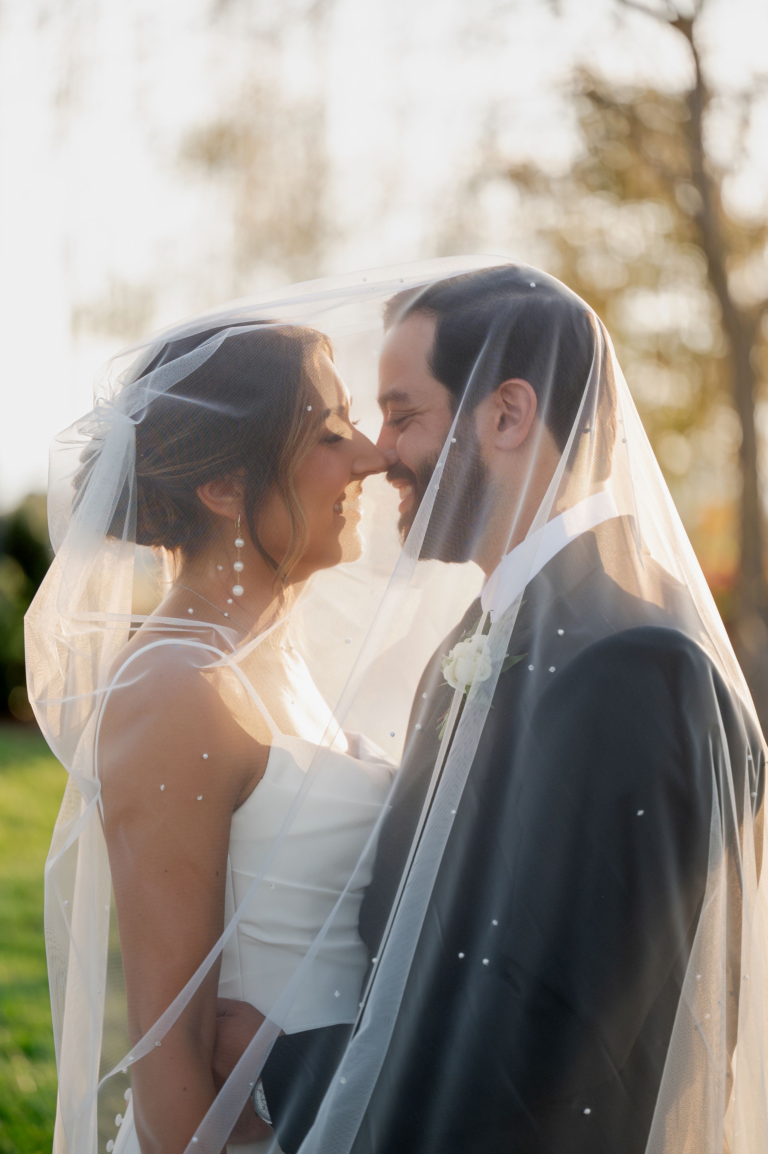 Romantic wedding couple embraces under flowing white veil during golden hour.