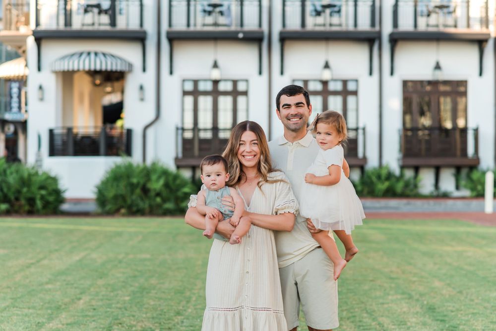 Family in coordinating neutral outfits posing together on green lawn in front of elegant historic building.
