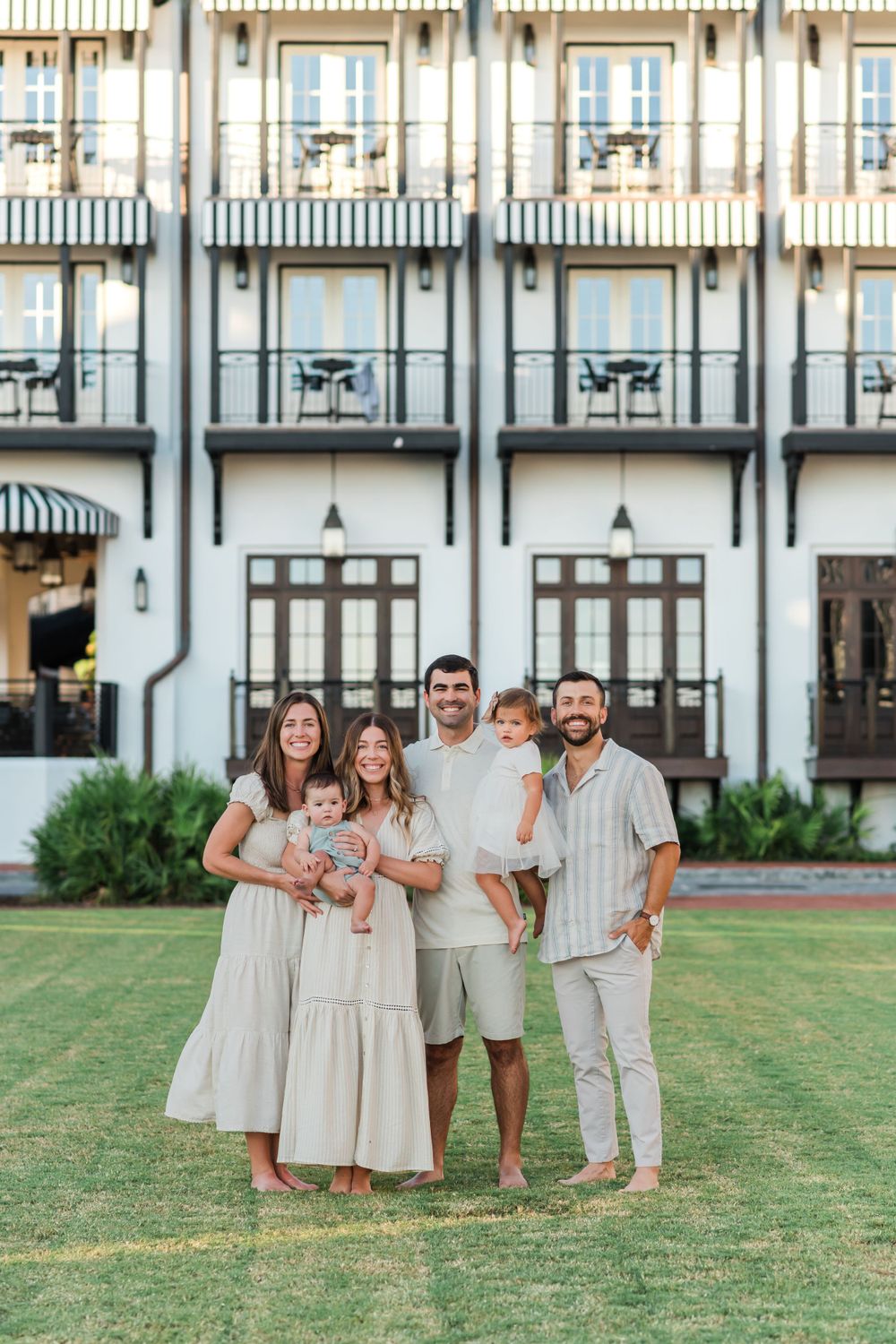 A group in coordinated cream and white outfits poses together on a grassy lawn in front of a historic building.