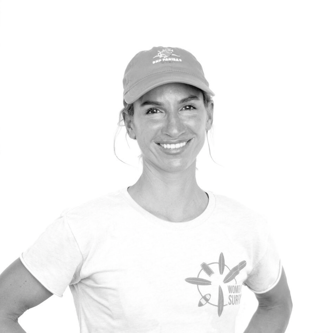 A black and white portrait of a smiling person wearing a baseball cap and white t-shirt with a compass design.