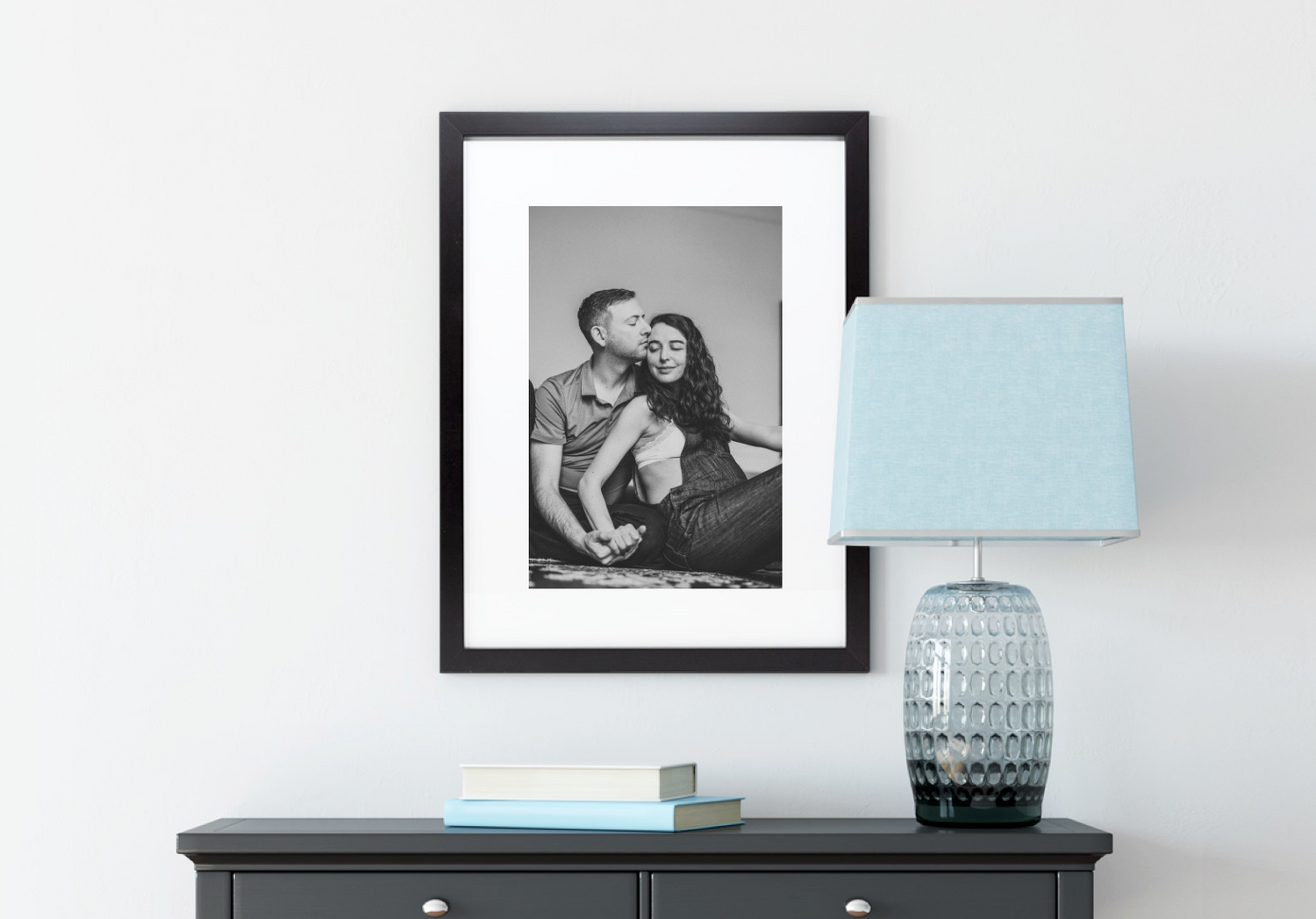 Black and white framed photo displayed above dark dresser with modern blue table lamp and decorative accents.