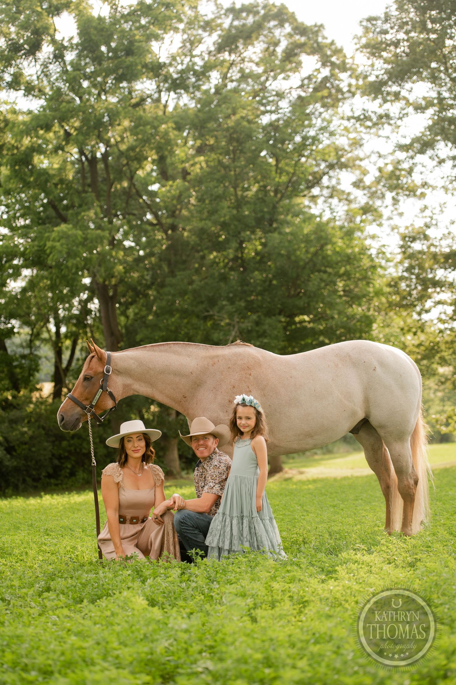A western-styled family photo featuring a pale horse in a sunlit meadow.