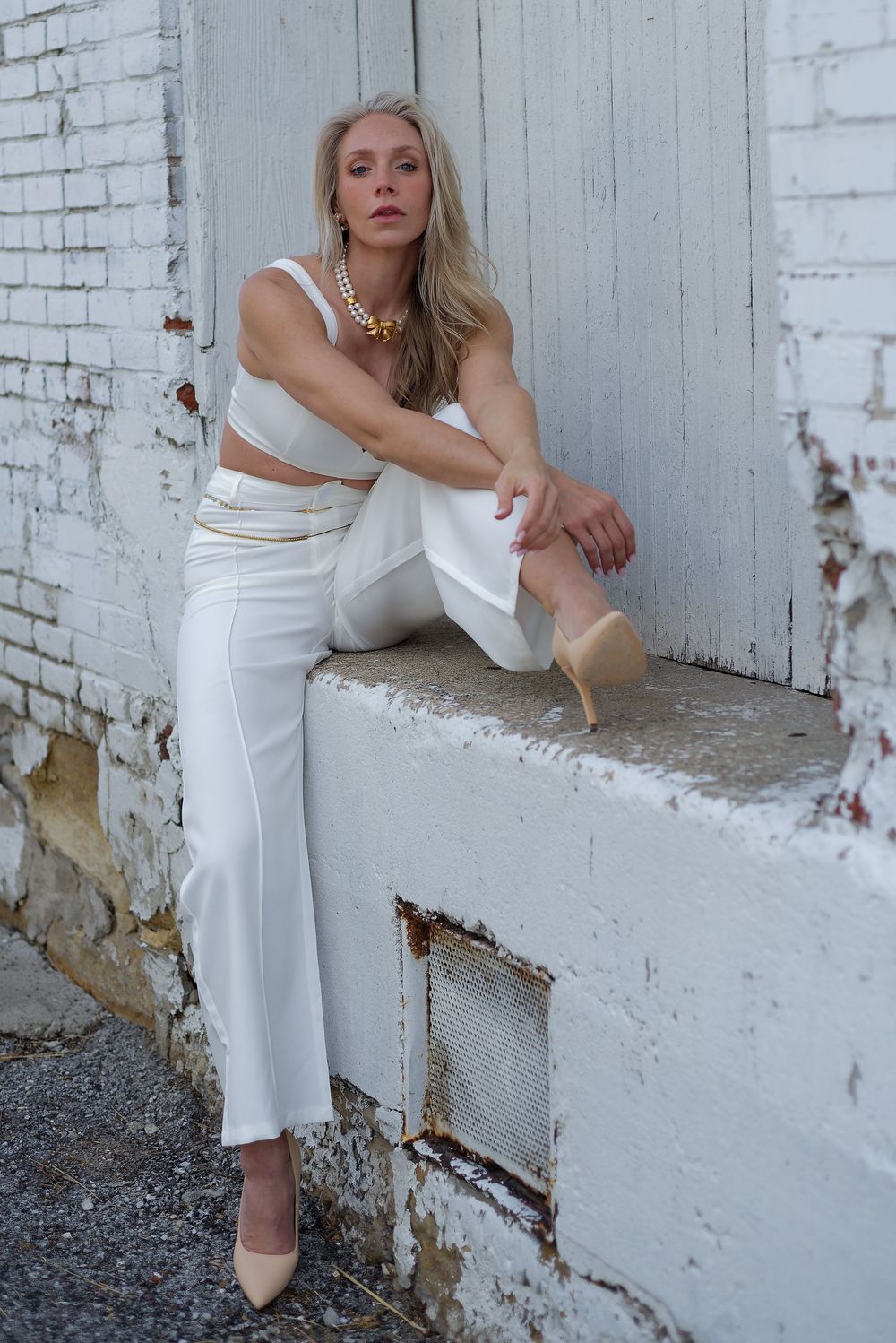Fashion model in white outfit poses against white brick wall showing different angles of minimalist ensemble.